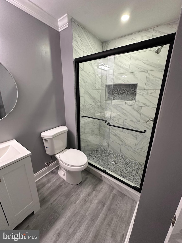 bathroom featuring toilet, hardwood / wood-style floors, walk in shower, crown molding, and vanity