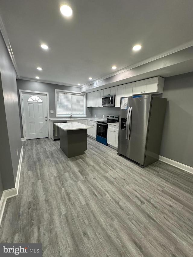 kitchen featuring hardwood / wood-style floors, appliances with stainless steel finishes, a center island, ornamental molding, and white cabinetry