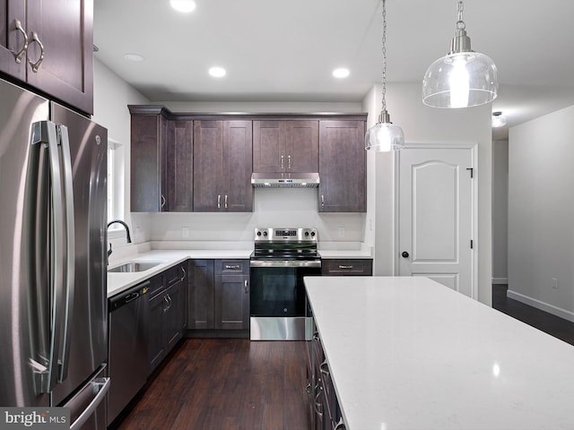 kitchen with appliances with stainless steel finishes, dark wood-style flooring, dark brown cabinets, under cabinet range hood, and a sink