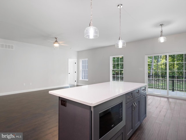 kitchen with visible vents, dark wood-style floors, a center island, built in microwave, and light countertops