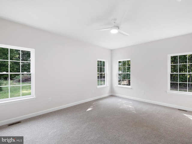 carpeted empty room with a ceiling fan, visible vents, plenty of natural light, and baseboards