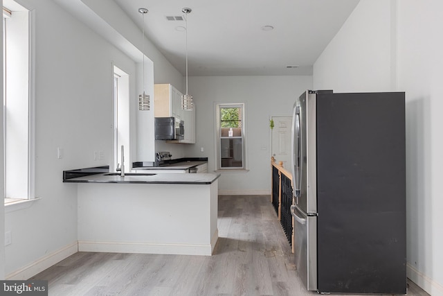 kitchen with baseboards, dark countertops, stainless steel appliances, light wood-style floors, and a sink