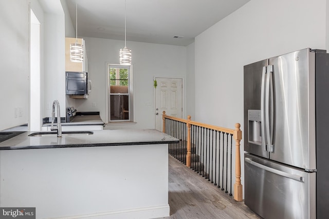 kitchen featuring stainless steel refrigerator with ice dispenser, light wood finished floors, a sink, dark stone counters, and a peninsula