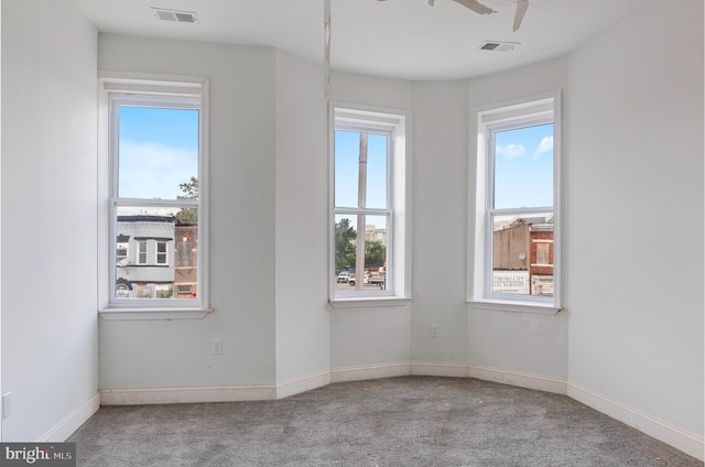 carpeted spare room featuring baseboards, visible vents, and ceiling fan