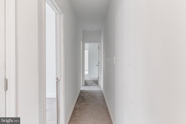 hallway with baseboards and light colored carpet