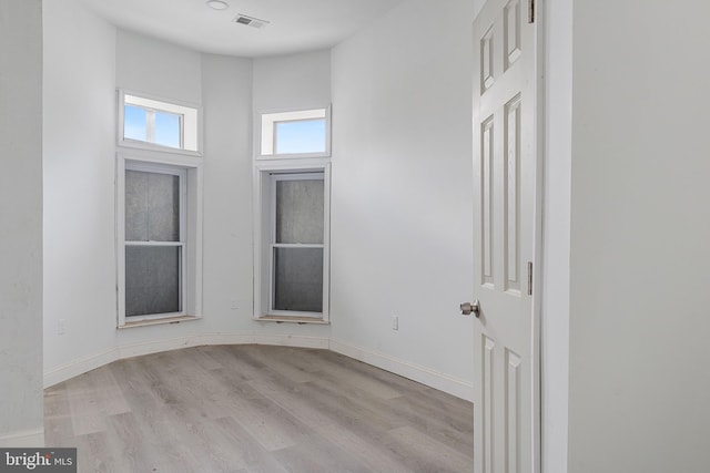 empty room featuring a towering ceiling, wood finished floors, visible vents, and baseboards