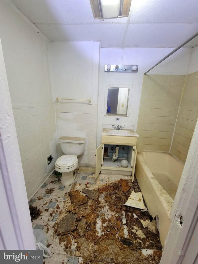 full bathroom with tile walls, toilet, sink, and a drop ceiling