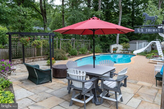 view of swimming pool with a shed, a patio, and a water slide