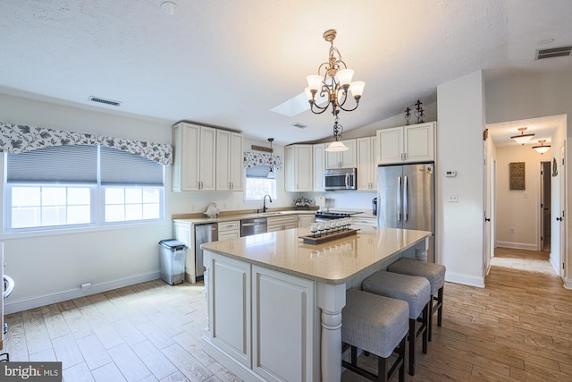 kitchen featuring appliances with stainless steel finishes, light wood-type flooring, a center island, pendant lighting, and lofted ceiling with skylight