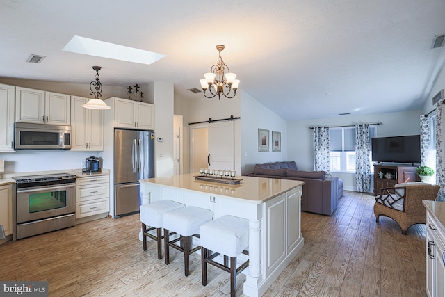 kitchen with light hardwood / wood-style flooring, stainless steel appliances, a center island, a barn door, and lofted ceiling with skylight