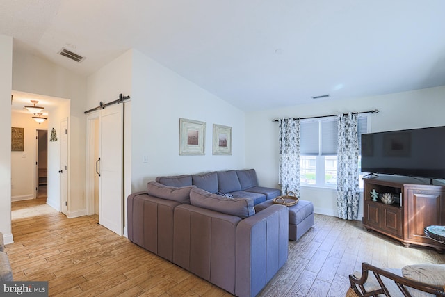 living room with vaulted ceiling, a barn door, and light hardwood / wood-style floors