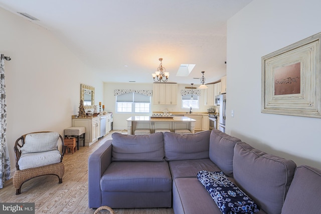 living room with sink, a notable chandelier, light hardwood / wood-style floors, and a skylight