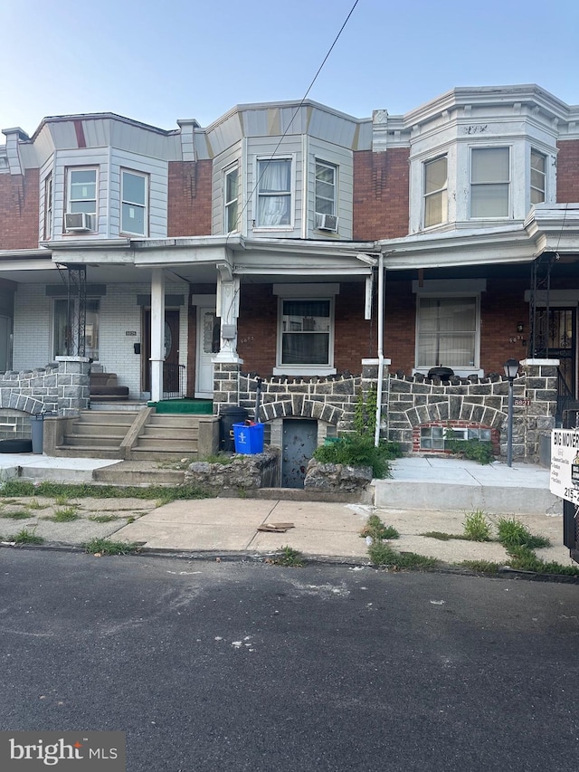 view of property featuring a porch, cooling unit, and brick siding