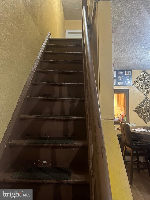 staircase with a textured ceiling and wood-type flooring