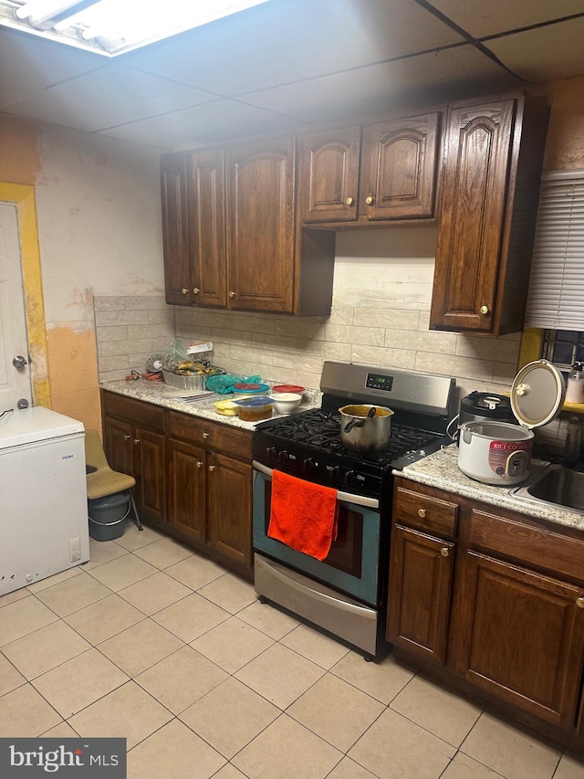 kitchen featuring white refrigerator, stainless steel gas range, dark brown cabinets, and light tile patterned flooring