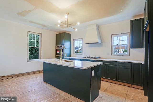 kitchen featuring a wealth of natural light, custom exhaust hood, an island with sink, and light hardwood / wood-style flooring