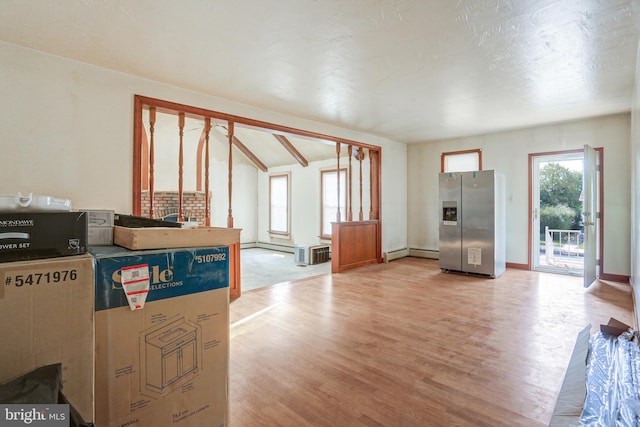 kitchen featuring baseboard heating, stainless steel fridge, a wall unit AC, and hardwood / wood-style flooring