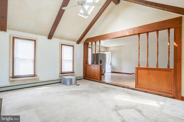 unfurnished living room with beam ceiling, a skylight, a baseboard heating unit, ceiling fan, and light wood-type flooring