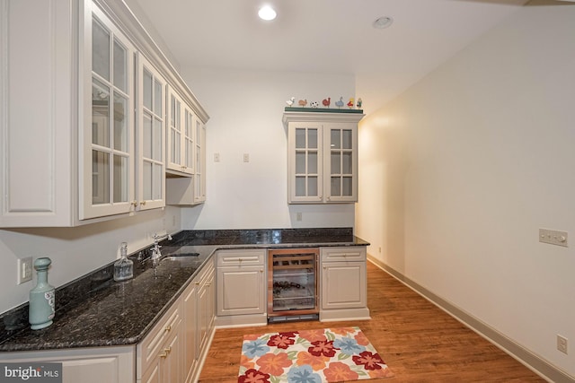 kitchen with dark stone counters, wood-type flooring, beverage cooler, and sink