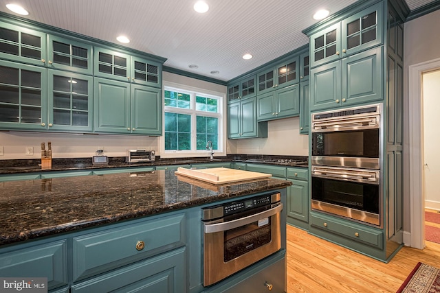 kitchen with stainless steel double oven, green cabinets, sink, and light hardwood / wood-style floors