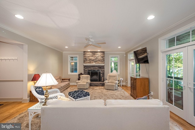 living room with light hardwood / wood-style floors, a stone fireplace, ornamental molding, and ceiling fan