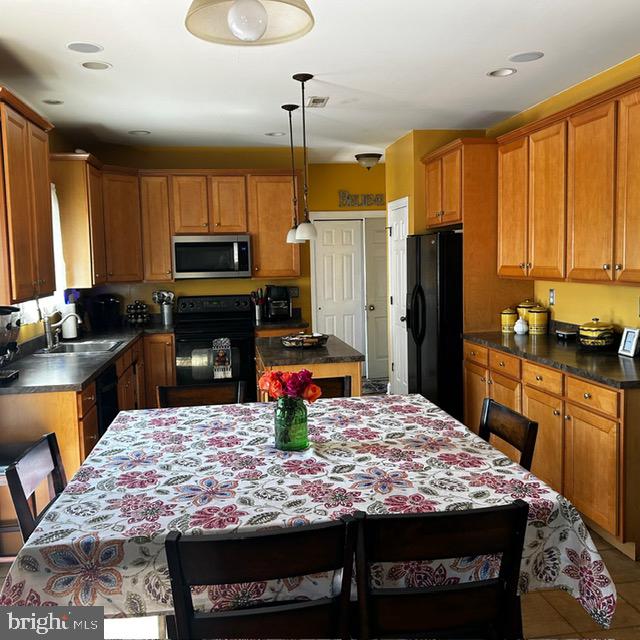 kitchen featuring tile patterned floors, decorative light fixtures, black appliances, a kitchen island, and sink