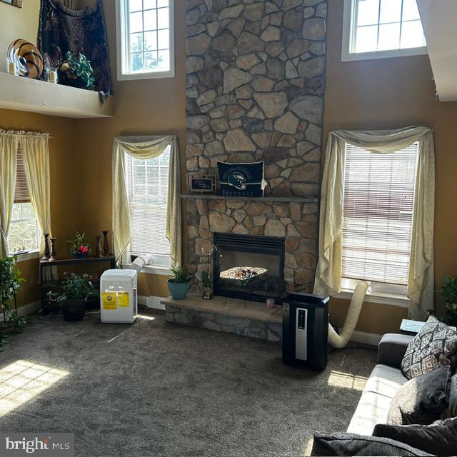 carpeted living room with a towering ceiling and a stone fireplace