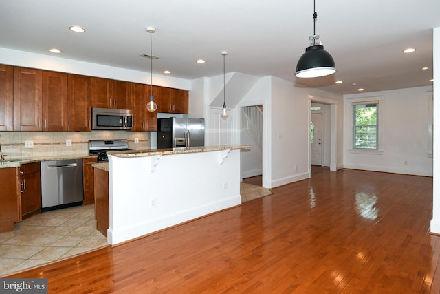 kitchen featuring hanging light fixtures, a center island, stainless steel appliances, light hardwood / wood-style floors, and a kitchen bar