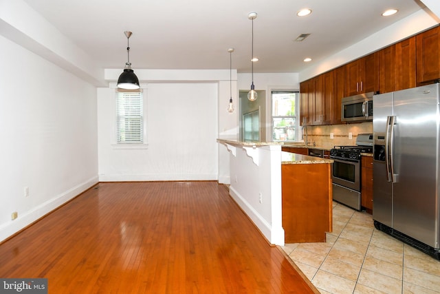 kitchen featuring light stone countertops, pendant lighting, stainless steel appliances, kitchen peninsula, and light wood-type flooring