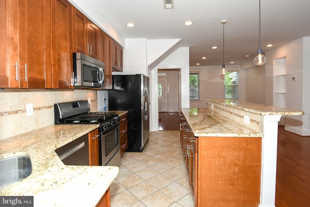 kitchen featuring light stone countertops, light tile patterned floors, appliances with stainless steel finishes, hanging light fixtures, and decorative backsplash