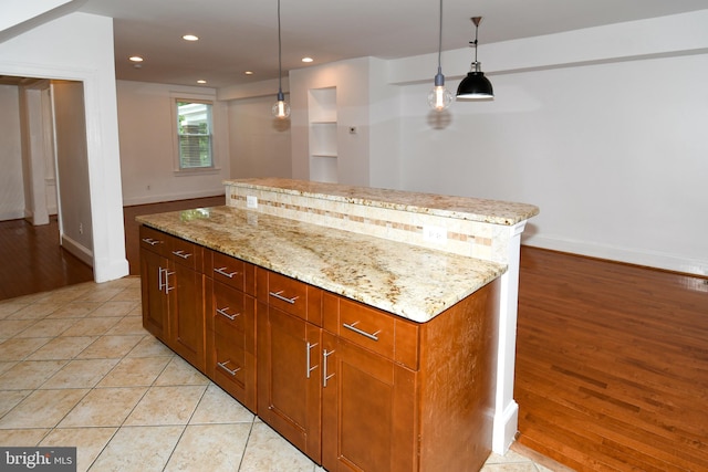 kitchen featuring hanging light fixtures, light stone countertops, light hardwood / wood-style flooring, and a center island