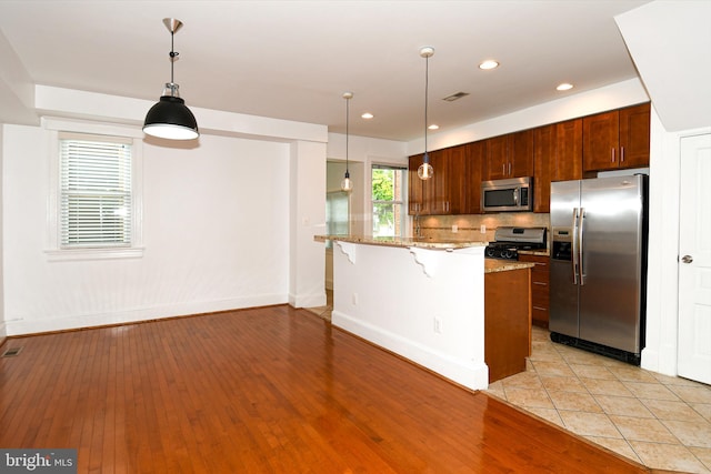 kitchen featuring light wood-type flooring, pendant lighting, stainless steel appliances, and light stone countertops