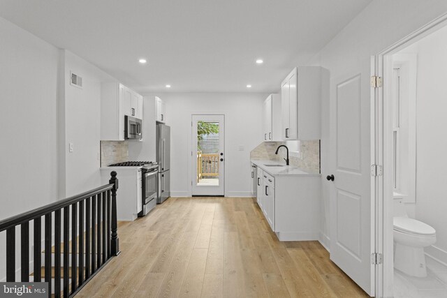 kitchen with stainless steel dishwasher, sink, white cabinets, and light hardwood / wood-style floors