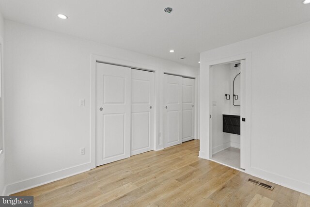 unfurnished bedroom featuring light hardwood / wood-style floors, multiple closets, and ensuite bath