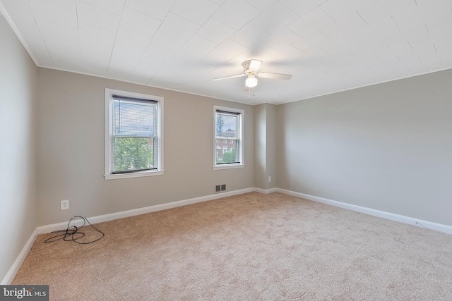 carpeted spare room with ornamental molding, baseboards, visible vents, and ceiling fan