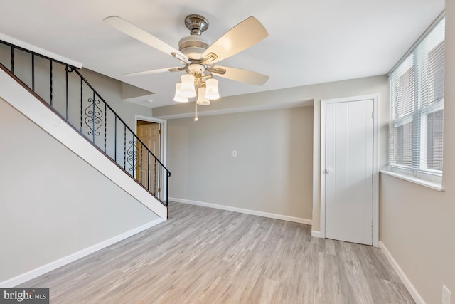 unfurnished living room featuring stairs, wood finished floors, baseboards, and a ceiling fan
