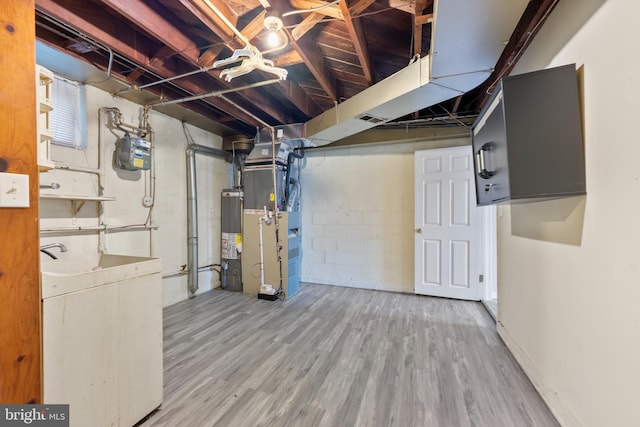 unfinished below grade area with heating unit, washer / clothes dryer, wood finished floors, water heater, and concrete block wall