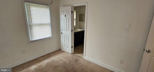 unfurnished bedroom featuring sink, light carpet, and ensuite bath