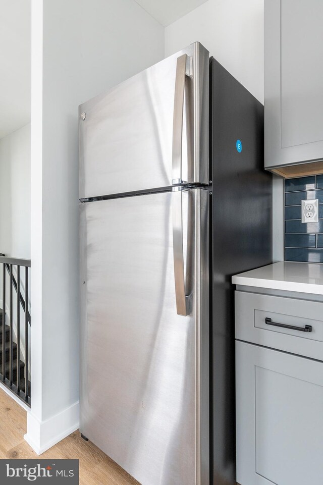 kitchen featuring light wood-type flooring, decorative backsplash, gray cabinets, and stainless steel refrigerator