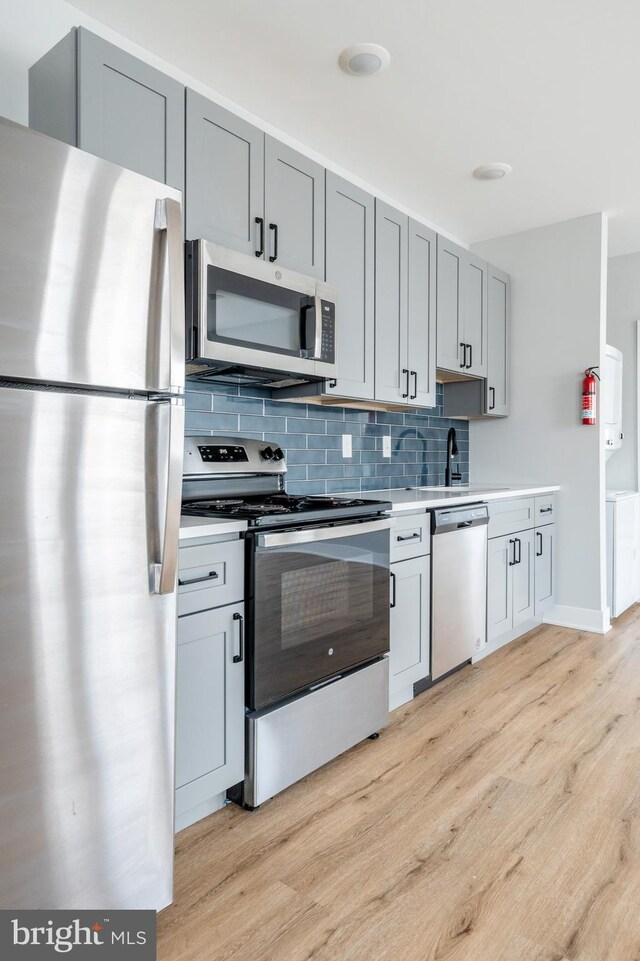 kitchen featuring light wood-type flooring, gray cabinets, appliances with stainless steel finishes, and decorative backsplash