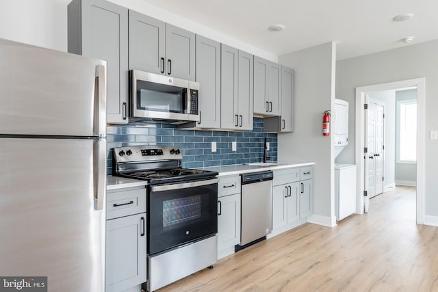 kitchen with backsplash, gray cabinetry, appliances with stainless steel finishes, and light hardwood / wood-style floors