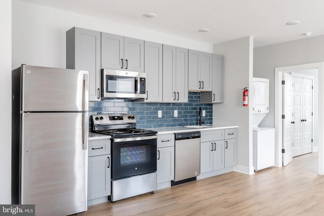 kitchen with backsplash, light hardwood / wood-style flooring, appliances with stainless steel finishes, sink, and stacked washer / drying machine