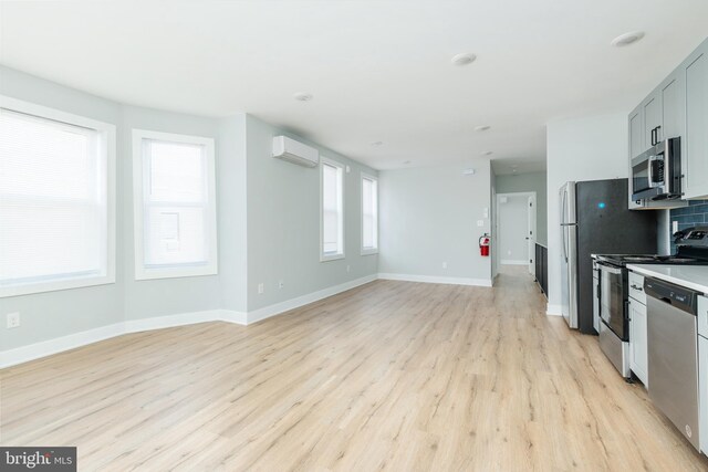 kitchen with light wood-type flooring, plenty of natural light, stainless steel appliances, and a wall mounted air conditioner