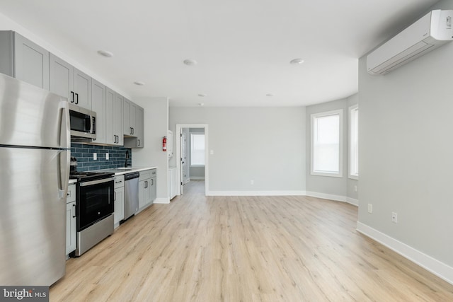 kitchen featuring a wall mounted AC, appliances with stainless steel finishes, backsplash, and light wood-type flooring