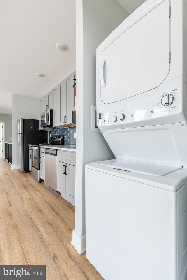 washroom with stacked washer / drying machine and light hardwood / wood-style floors