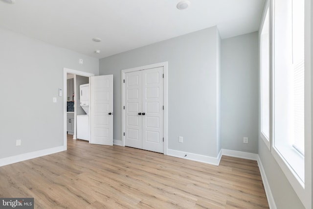 unfurnished bedroom featuring stacked washer and clothes dryer and light hardwood / wood-style flooring