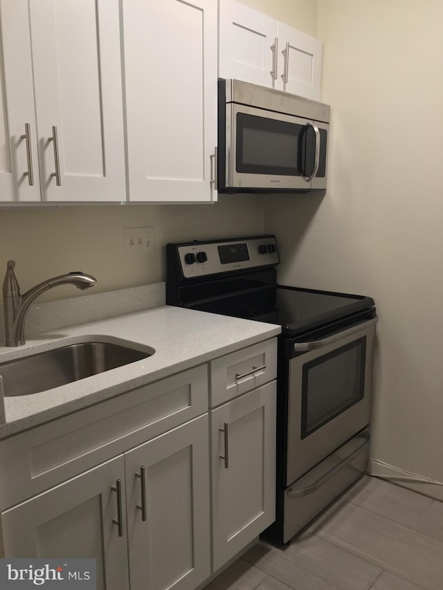 kitchen with light stone countertops, white cabinetry, sink, and stainless steel appliances