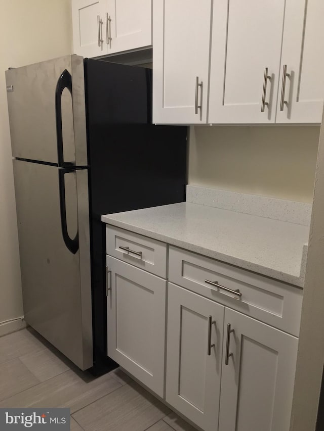 kitchen featuring white cabinetry, light stone counters, and stainless steel refrigerator