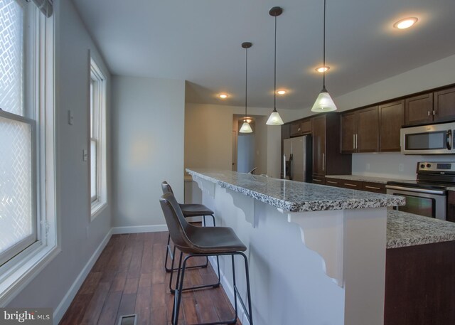 kitchen featuring dark hardwood / wood-style flooring, light stone counters, a kitchen bar, and stainless steel appliances