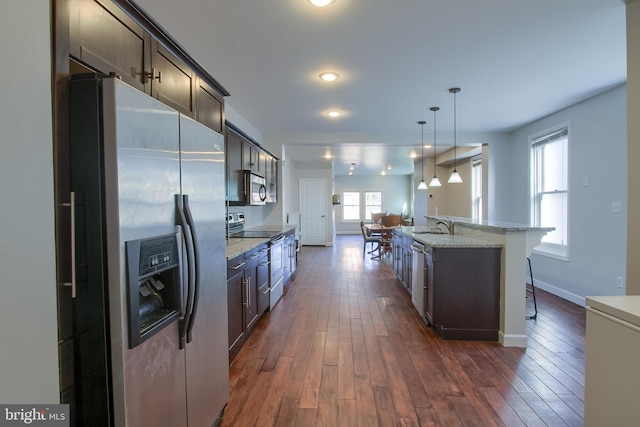 kitchen featuring dark hardwood / wood-style flooring, dark brown cabinets, a kitchen island with sink, and appliances with stainless steel finishes